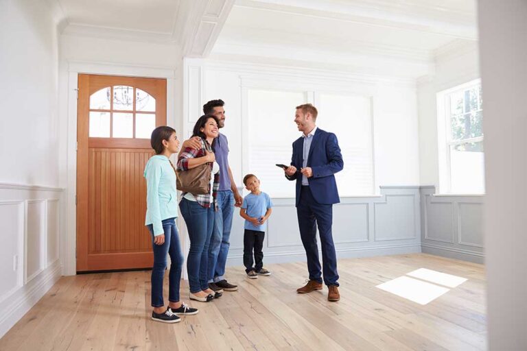 A real estate agent reviews paperwork with a couple in a home filled with natural light and typical Midwestern furnishings.